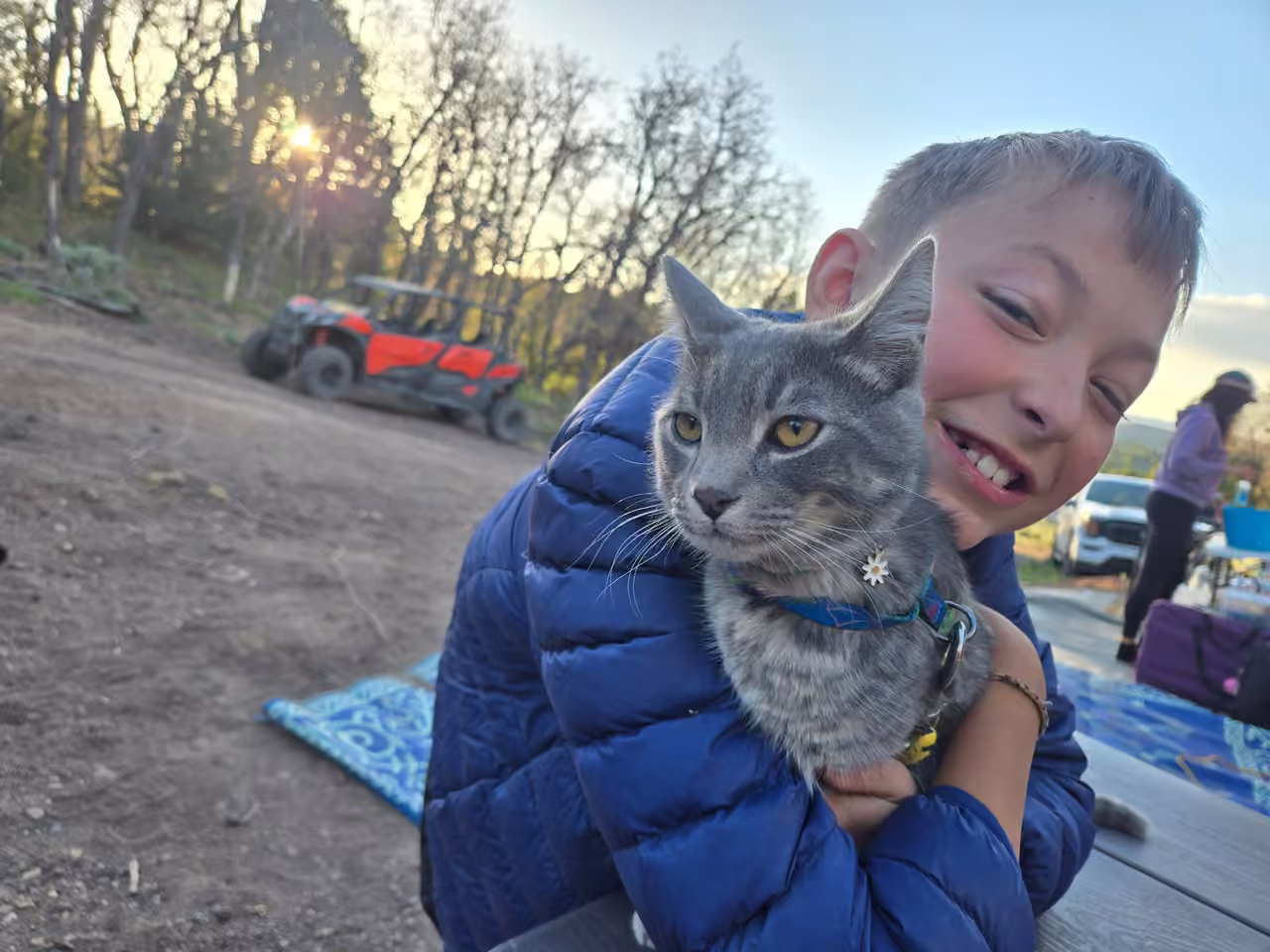 Kid hugging a gray cat at a Starlit Ridge campsite at sunset