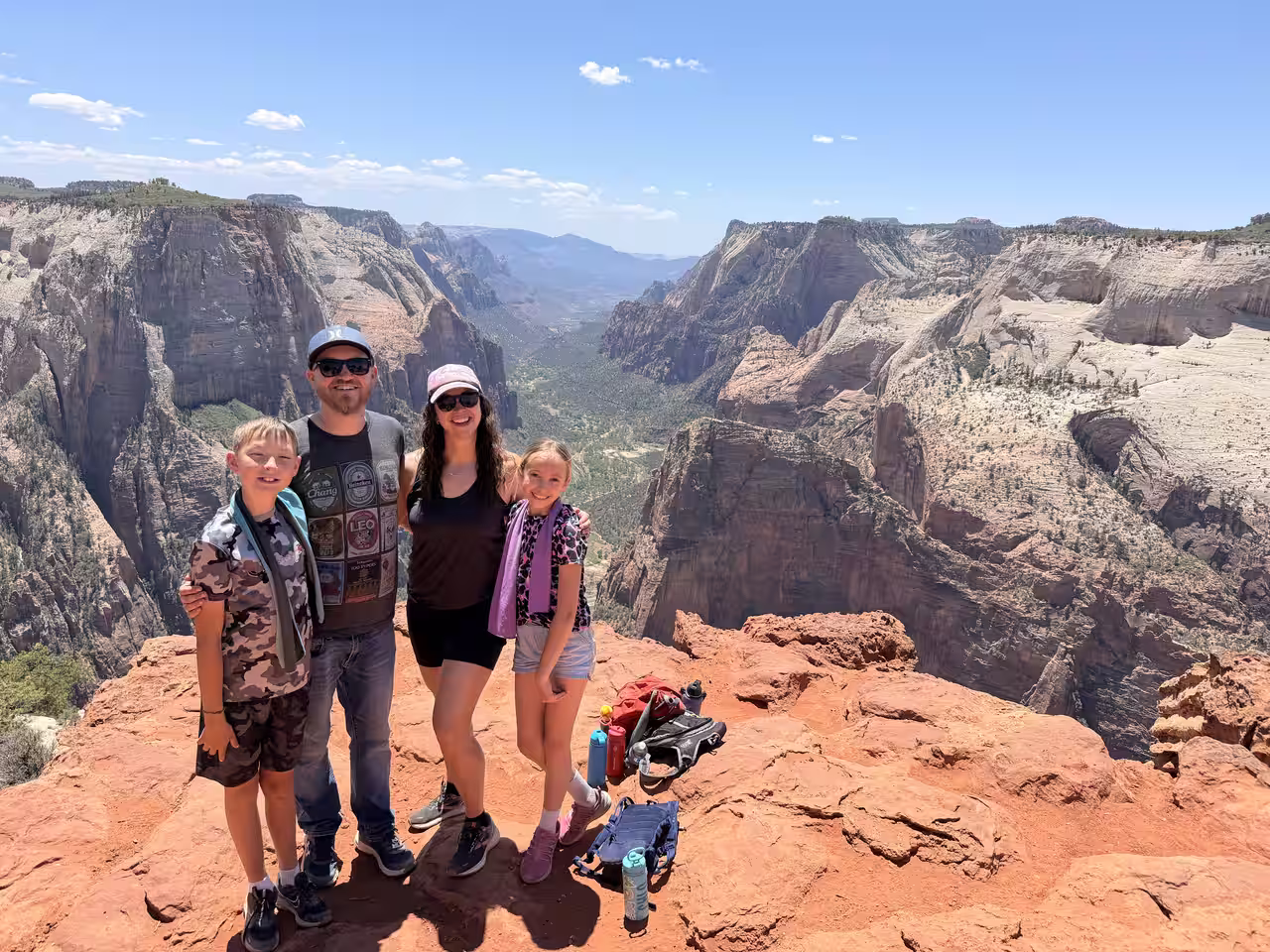 Family of four posing at the Observation Point summit with Zion Canyon in the background